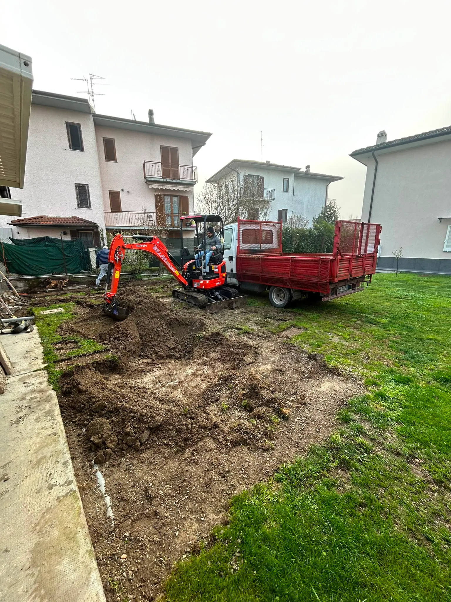 Mini escavatore e autocarro durante uno scavo in giardino